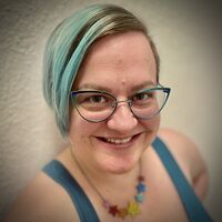 Biddy is a queer, white woman with glasses, blue hair, and a rainbow necklace